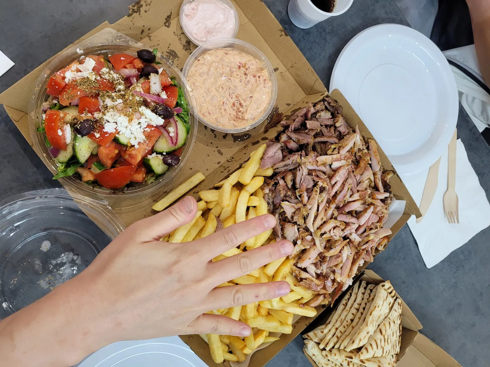 Overhead of Bayside Pack with lamb, chips, Greek salad and dips with a customer's hand reaching in
