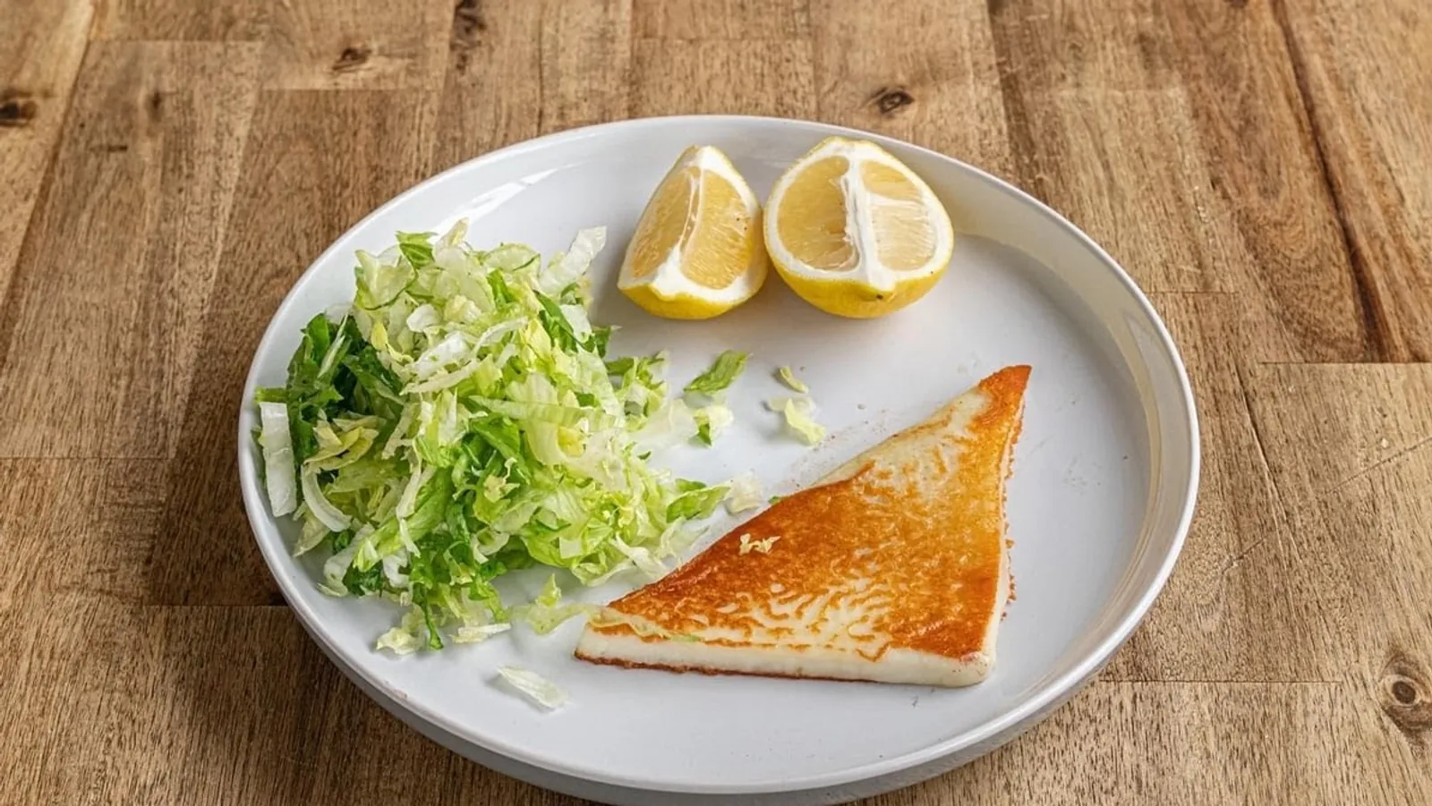 Saganaki fried cheese with shredded lettuce and lemon wedges on a white plate