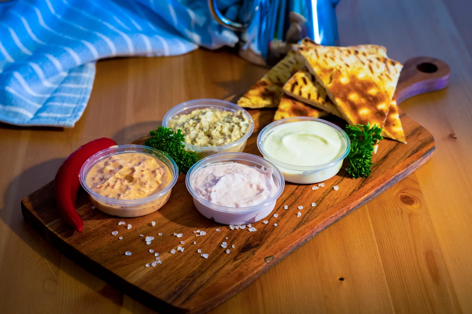 Greek dip taster board with four ramekins, grilled pita, red chilli and sea salt on dark wood