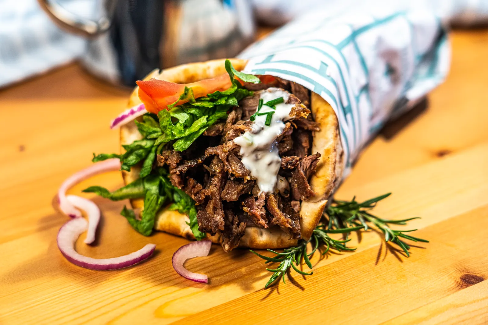 Charcoal lamb souvlaki wrap with tzatziki, lettuce and red onion on a wooden board with rosemary