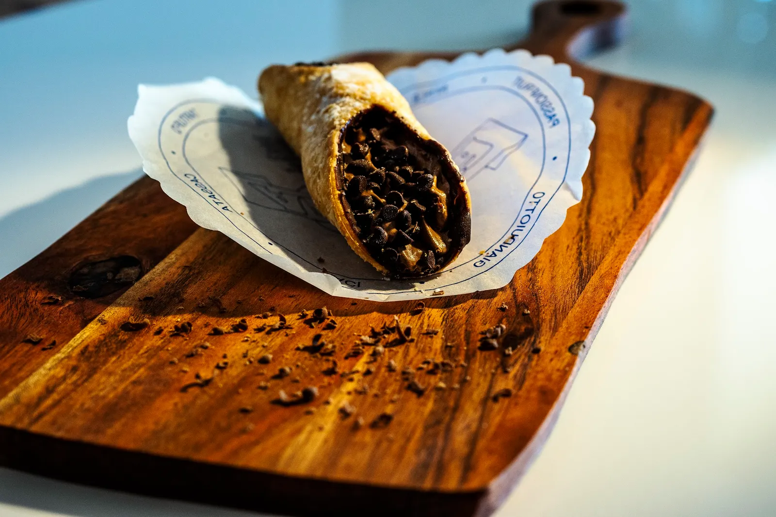 Chocolate cannoli on a dark wooden board with chocolate shavings and a paper doily
